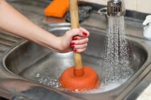 A woman using a plunger on a kitchen sink.