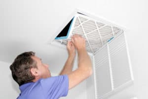 A man removing an air filter from a spot in a ceiling.