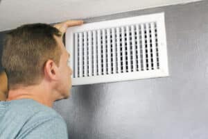 A man inspecting an air vent in a home.