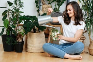 A smiling woman sitting on the ground and watering a plant.